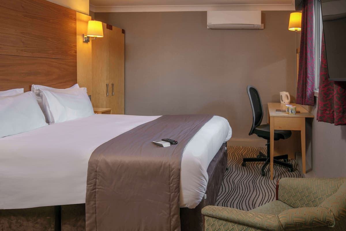 A hotel room with a large bed, a desk, a chair, and a TV.