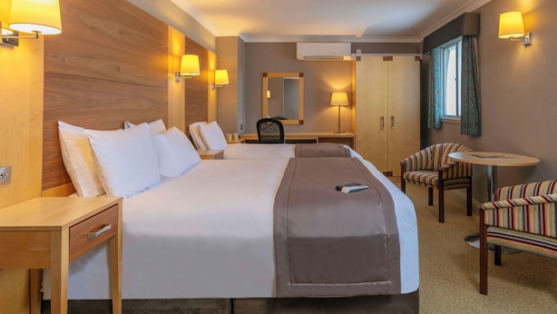 Ein Hotelzimmer mit einem großen Bett, Nachttischen, einem Schreibtisch, einem Sessel, einem kleinen runden Tisch und einem Spiegel.