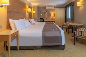 Une chambre d’hôtel avec un grand lit, des tables de chevet, un bureau, une chaise, une petite table ronde et un miroir.