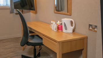 Ein Hotelzimmer mit einem Holztisch, einem schwarzen Bürostuhl, einem Flachbildfernseher, einer Kaffeemaschine und einer Kaffeetasse.