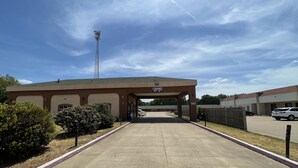A building with a clear entrance, a parking lot, and a fenced area with vehicles. - Gun Barrel Executive Inn (Mabank)