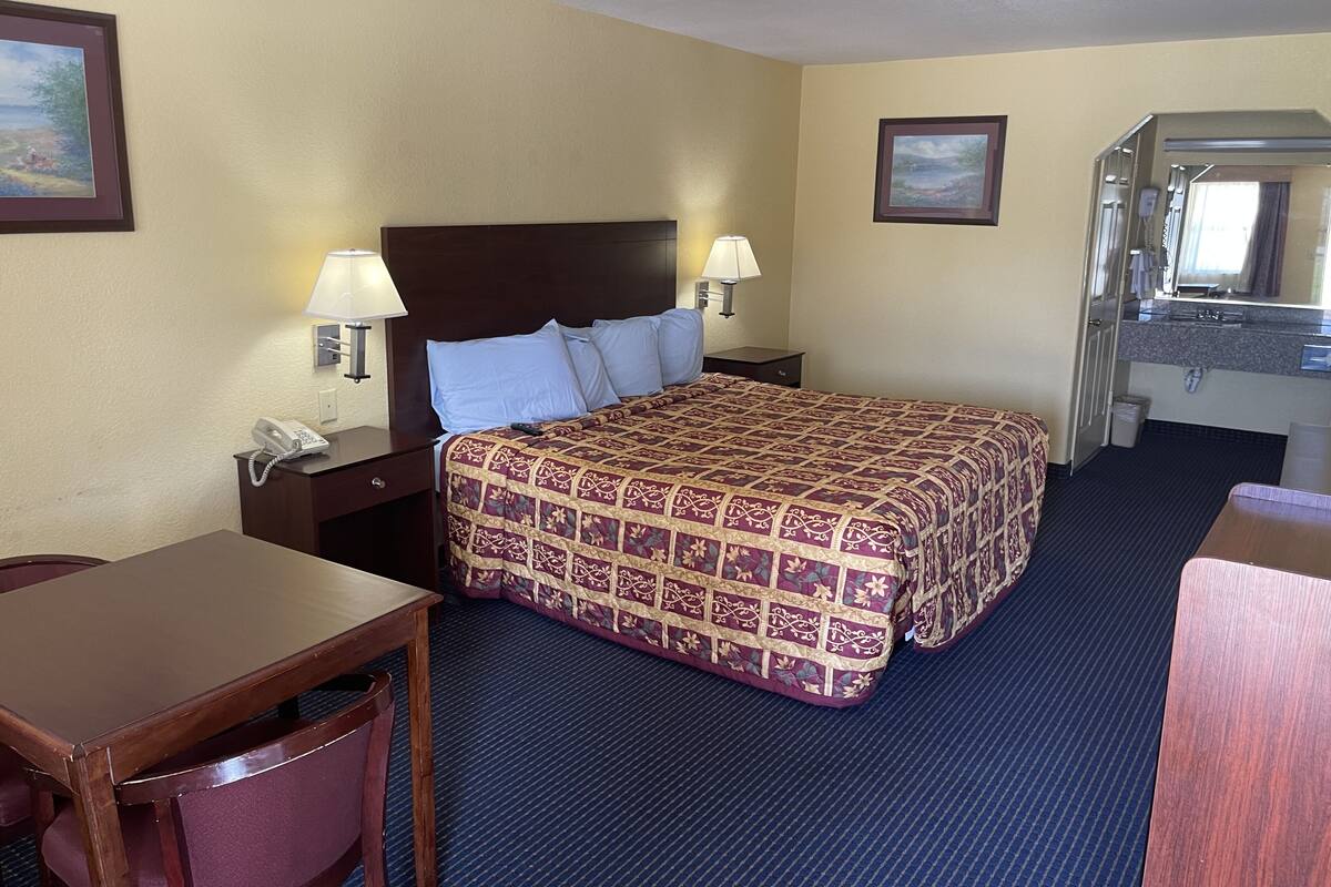 A hotel room with a large bed, two bedside tables with lamps, a desk with a chair, and a bathroom with a mirror and sink.