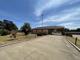 Entrada de un hotel con un letrero que dice Executive Inn & Suites, un estacionamiento y una alta torre de comunicaciones al fondo.