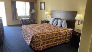 A hotel room with a large bed, two bedside lamps, a desk with a chair, and a window with curtains. - Gun Barrel Executive Inn (Mabank)