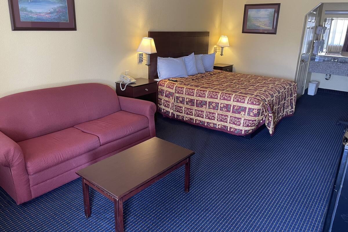A hotel room with a bed, a red sofa, a small table, two bedside lamps, and a framed picture on the wall.