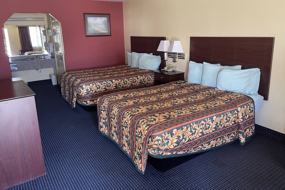 A hotel room with two beds, a desk, a mirror, and a nightstand with a lamp.