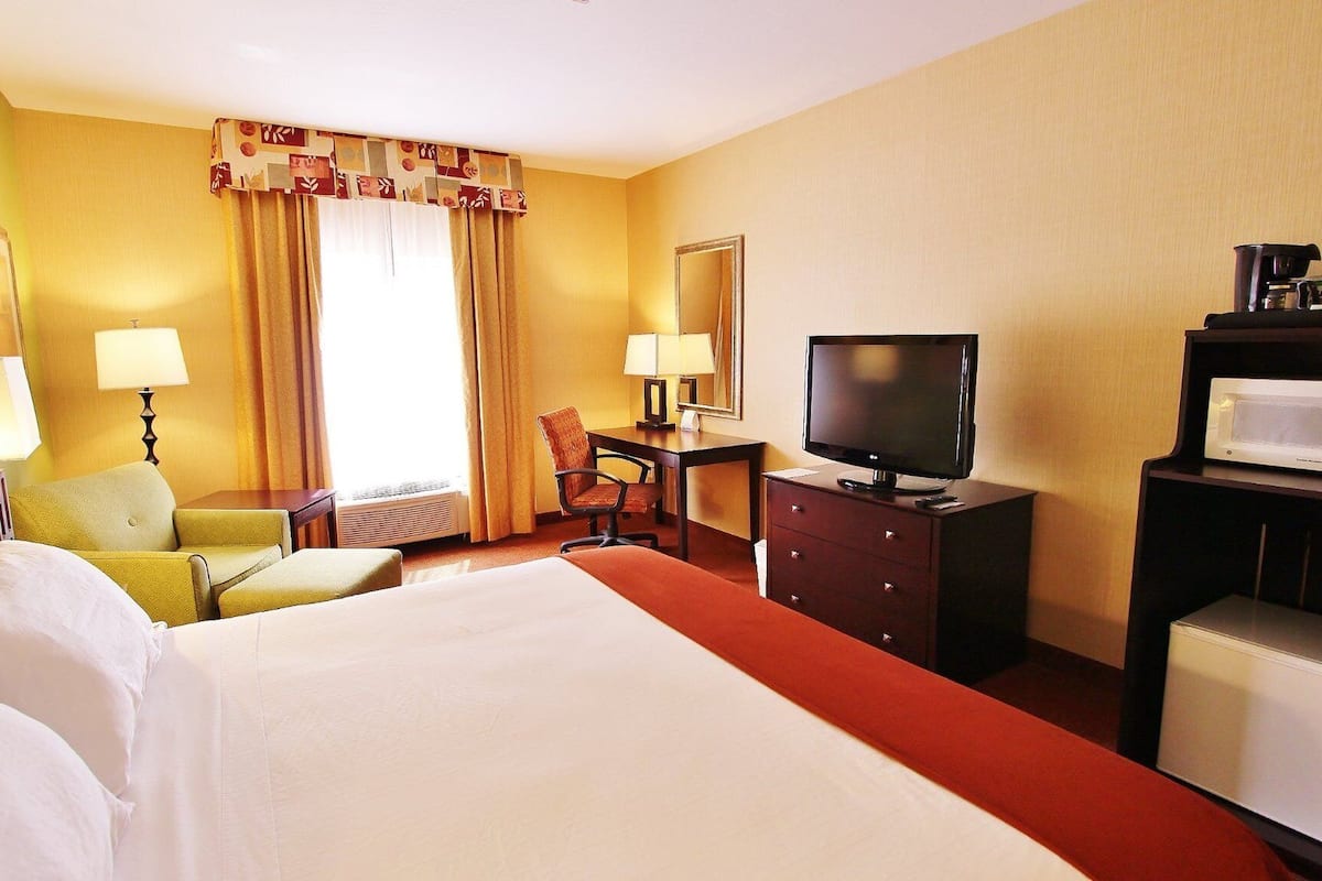 A hotel room with a large bed, a desk with a television, a microwave, and a chair.