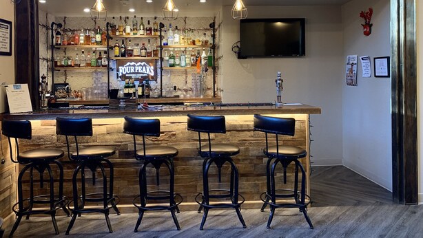 Een bar met een houten toog, meerdere krukken en een diversiteit aan flessen en glazen.