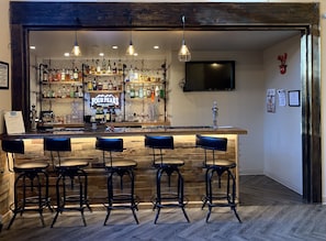 A bar area with a wooden bar counter, multiple stools, and a variety of bottles and glasses. - GreenTree Inn & Suites in Pinetop (Pinetop)