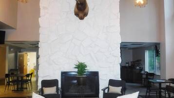 A lobby with a stone wall, a mounted deer head, a seating area with leather sofas and a table, and hanging pendant lights.