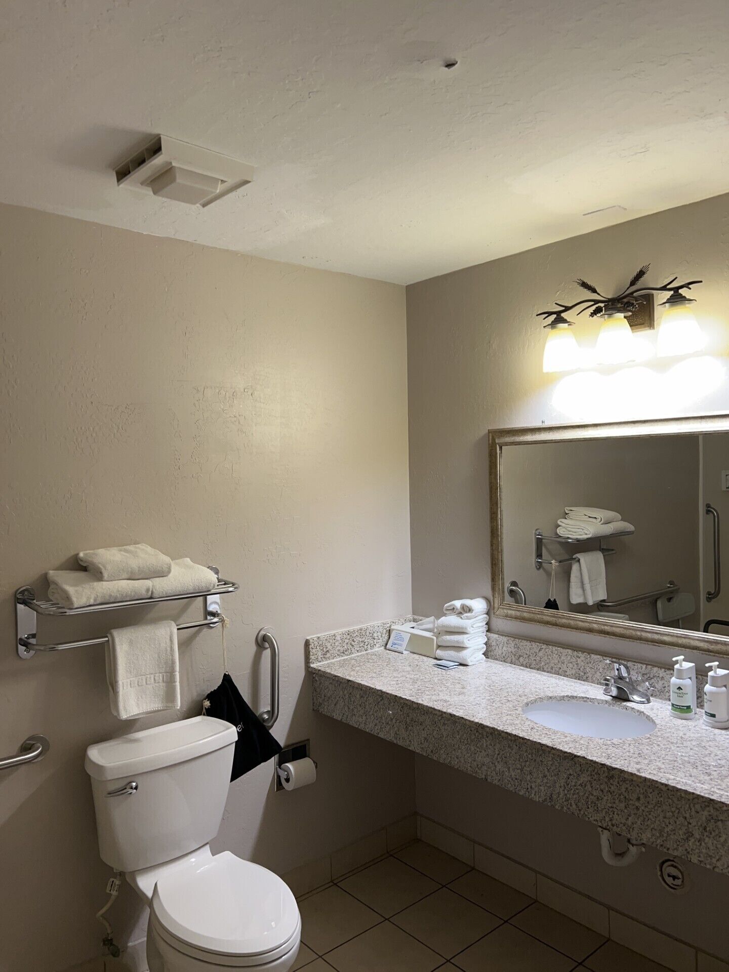 A bathroom with a toilet, sink, towel rack, and a mirror with lights.