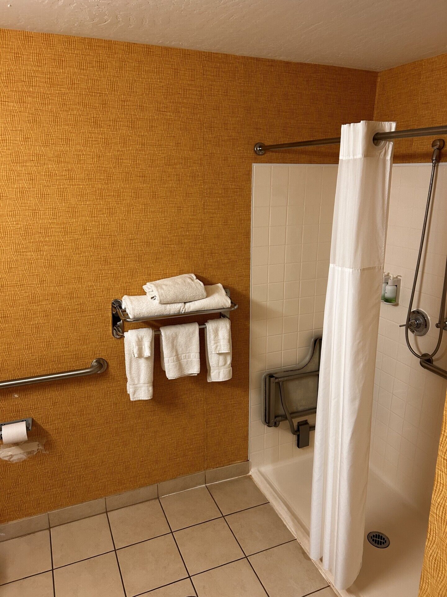 A bathroom with a patterned wall, a shower with a curtain, and a towel rack with towels.