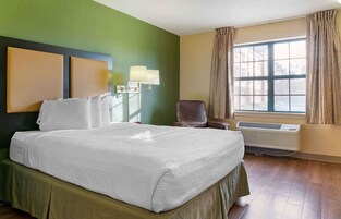 Habitación de hotel con una cama grande, una silla, una lámpara, una ventana con cortinas y un equipo de aire acondicionado.