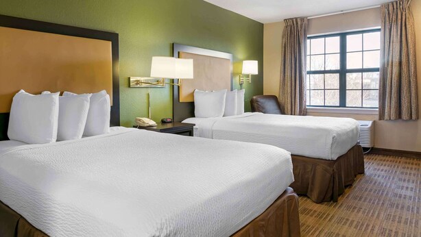 A hotel room with two beds, a large window with curtains, a desk with a lamp, and a chair. - Extended Stay America Select Suites Detroit Farmington Hills (Farmington Hills)