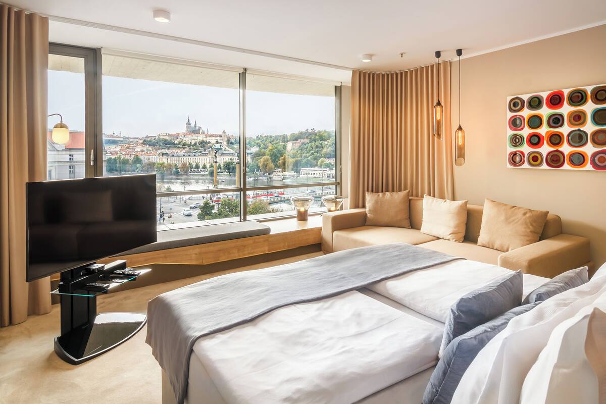 Quarto de hotel com uma janela grande, uma cama, uma televisão e uma obra de arte na parede.