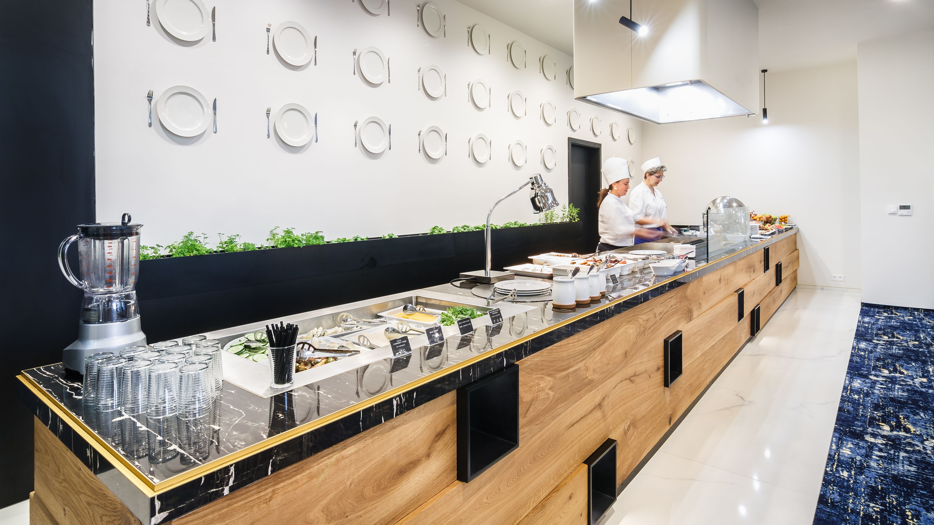 Uma mesa de buffet moderna com bancada de mármore, liquidificador e diversos recipientes com alimentos.