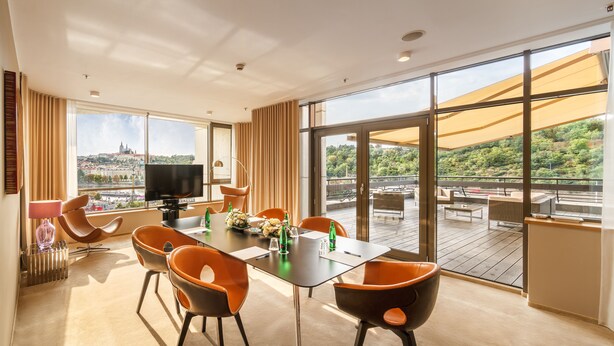 A modern hotel room with a large balcony, a dining area, and a television. - The President (Prague)