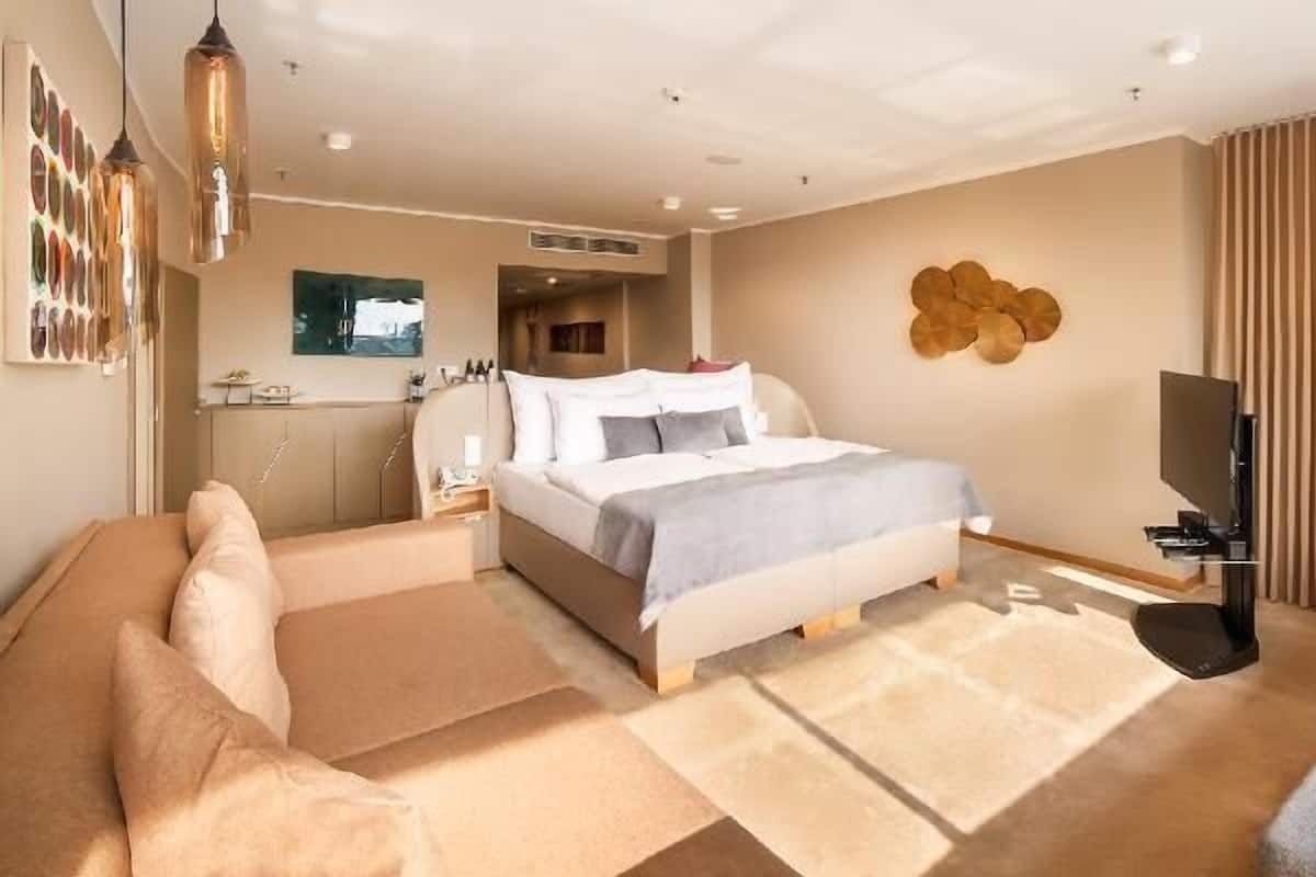 Quarto de hotel com cama, sofá, televisão e uma obra de arte na parede.