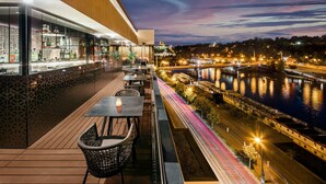 A rooftop bar with a view of a river and city lights at dusk. - The President (Prague)
