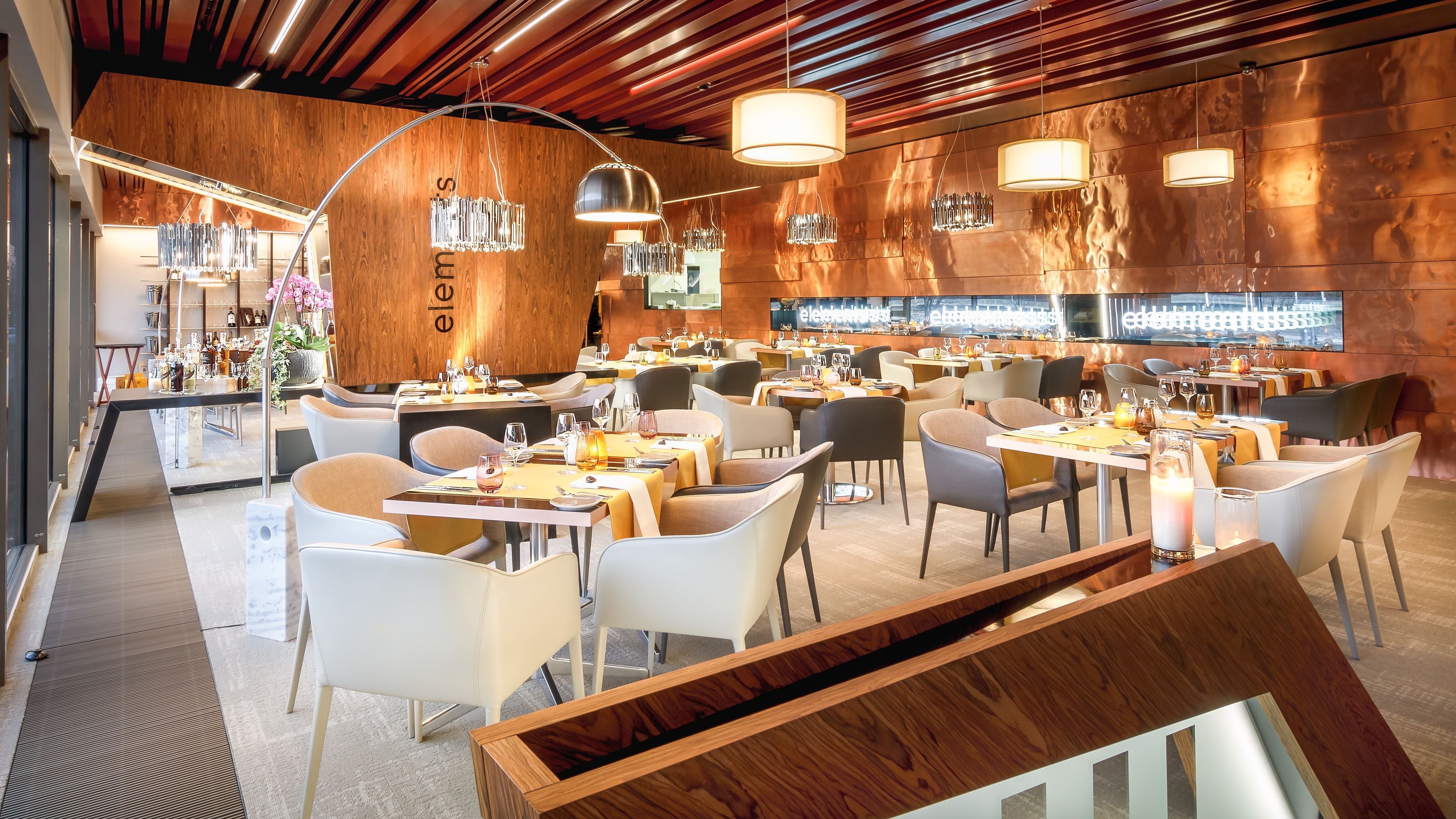 Um restaurante moderno com detalhes em madeira, mobiliário contemporâneo e um espaço de bar.