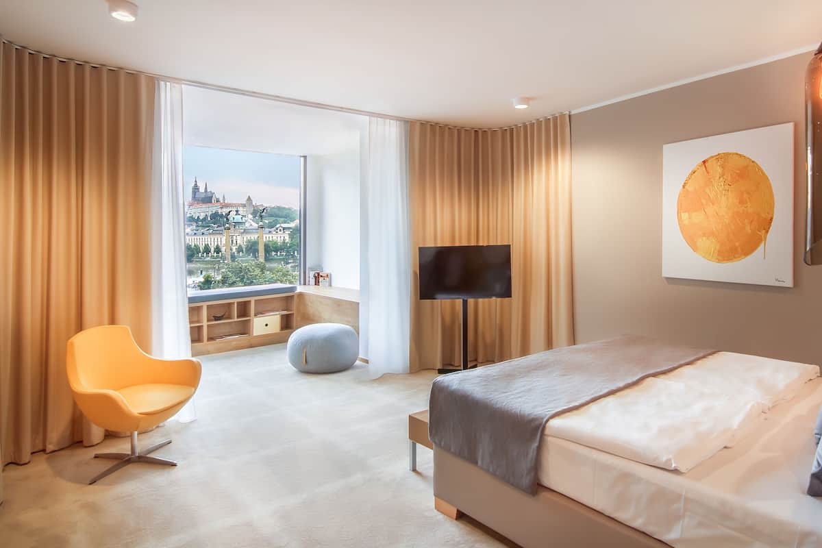 Quarto de hotel moderno com uma cama grande, televisão e vista para a paisagem urbana.