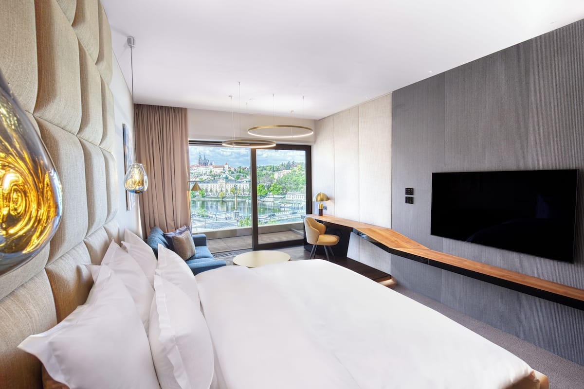 Quarto de hotel moderno com uma cama grande, uma escrivaninha, televisão de tela plana e vista para a cidade através de amplas janelas.