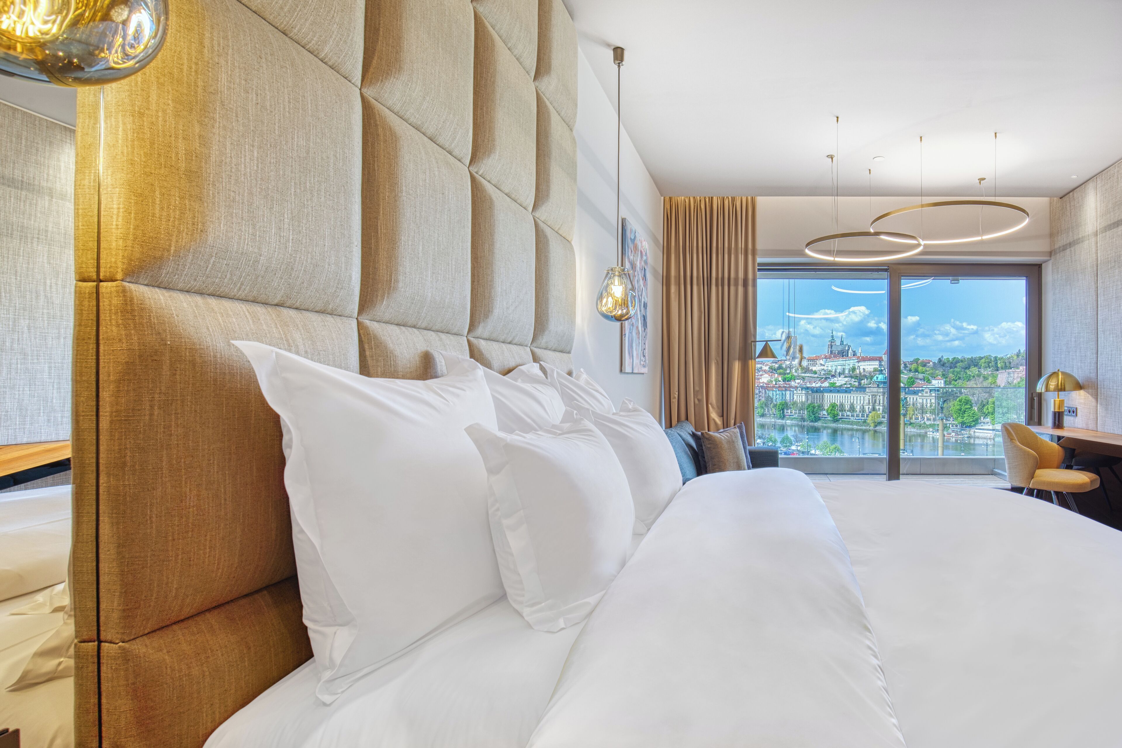 Quarto de hotel com uma cama grande, vista para o horizonte urbano e um lustre moderno.