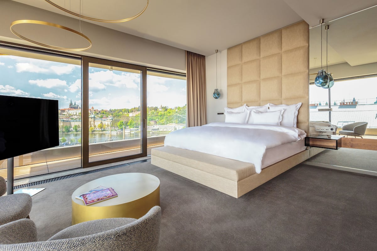 Quarto de hotel moderno com uma cama grande, televisão, mesa de centro redonda e vista para a paisagem urbana.