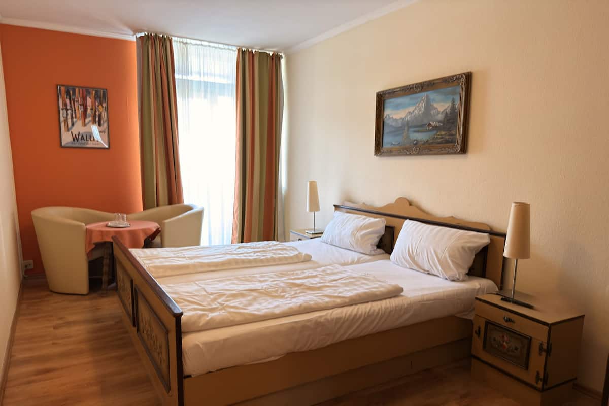 A hotel room with a double bed, a small table, a chair, a nightstand, and a painting on the wall.