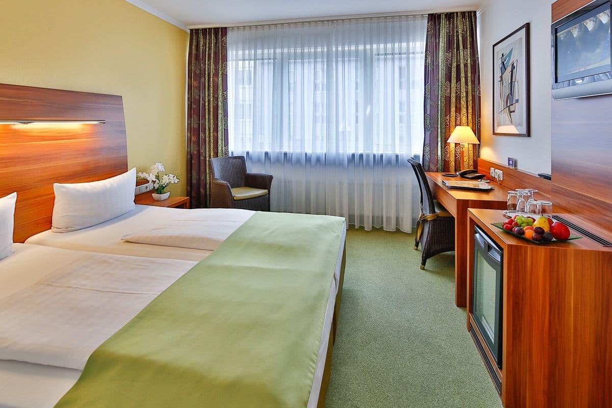 A hotel room with a large bed, a desk with a lamp, a chair, and a television.
