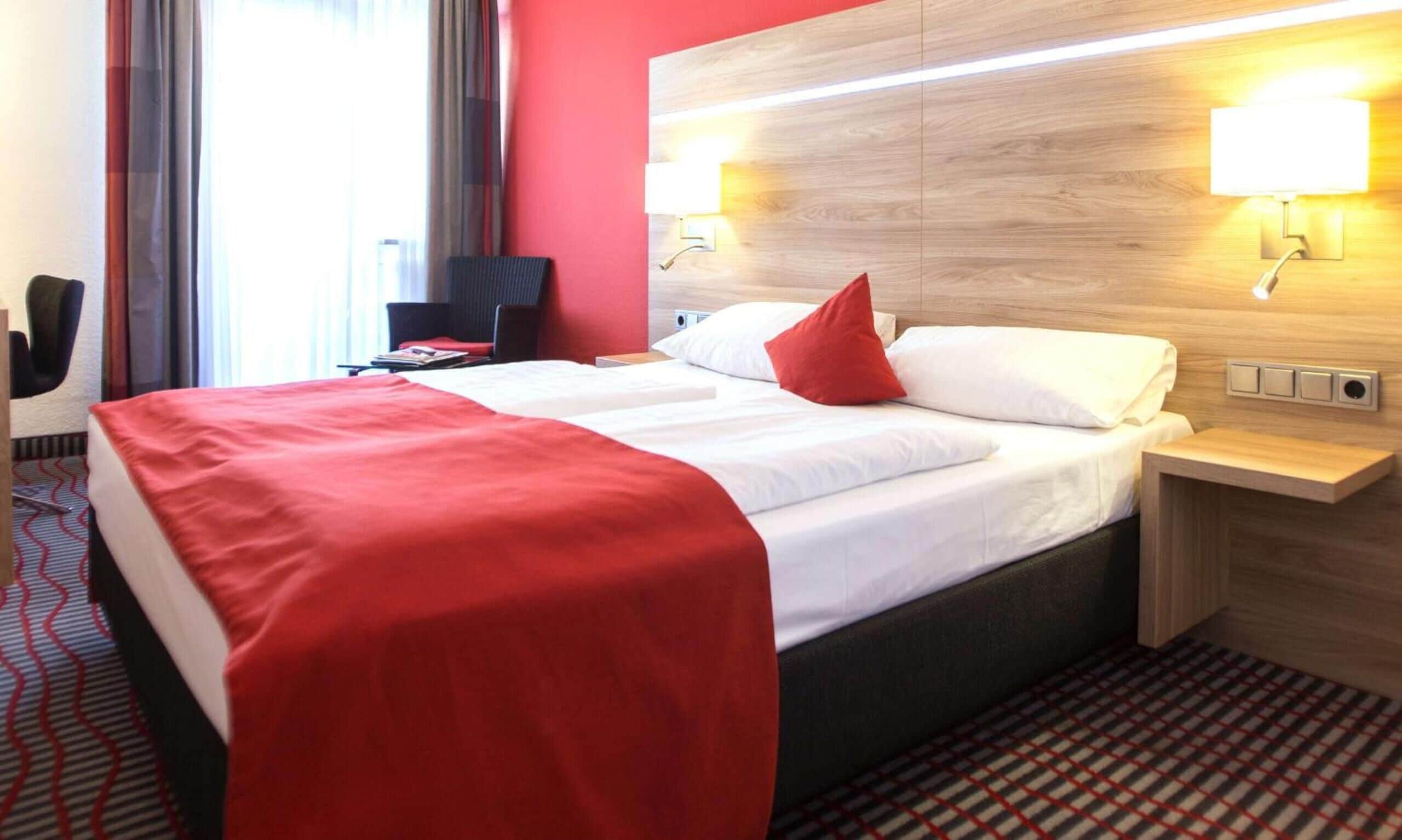 A hotel room with a bed, a desk, a chair, and a window with curtains.