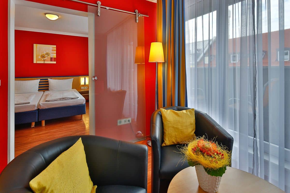 A hotel room with a bed, two bedside tables, a chair, a table with a vase, and a window with curtains.