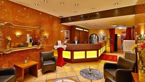 Un hall d’hôtel comprenant un comptoir d’accueil, des fauteuils en cuir, un grand miroir et un motif décoratif sur le sol.