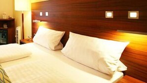 Une chambre d’hôtel avec une tête de lit en bois, deux oreillers blancs, une lampe de chevet et une table de chevet avec une lampe.