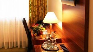 Une chambre d’hôtel avec un bureau en bois, une lampe, un arrangement floral et un téléviseur fixé au mur.