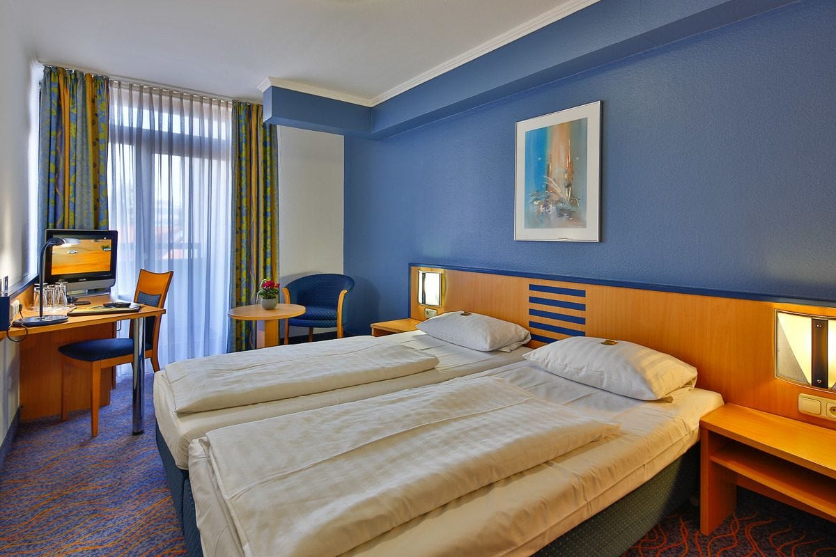 A hotel room with a large bed, a desk with a computer, a chair, and a small table.