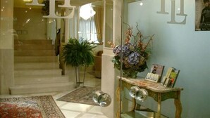 A hotel lobby with a glass partition, a staircase, a decorative plant, and a small table with books. - Hotel San Luca (Verona)