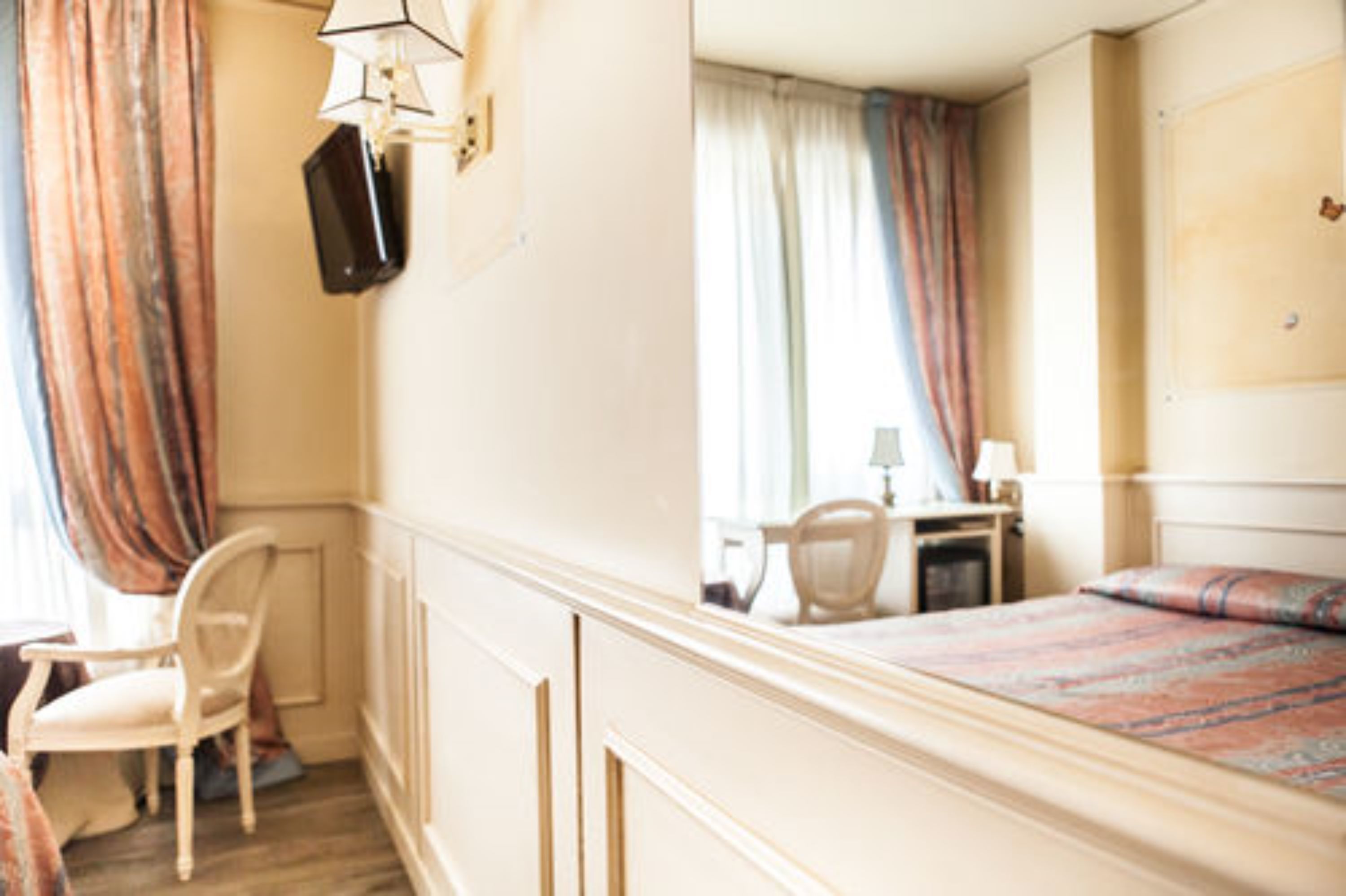 Habitación de hotel con cama, escritorio, silla y televisor montado en la pared.