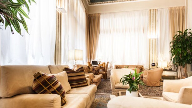 A spacious living room with beige sofas, a coffee table, and a potted plant. - Hotel San Luca (Verona)