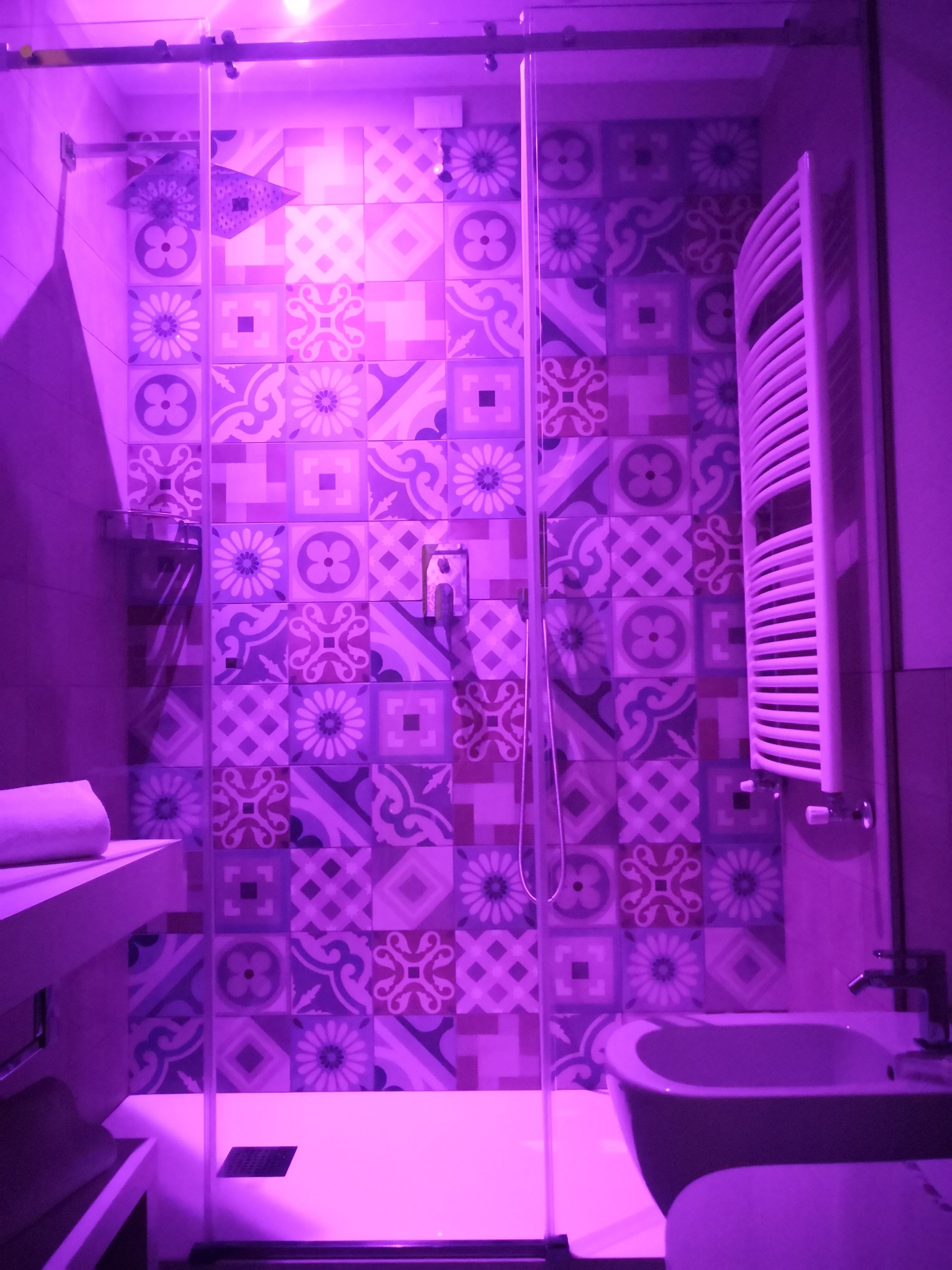 Een badkamer met patroon betegelde vloer, een glazen douchecabine, een wit wastafelmeubel en een handdoekhouder.