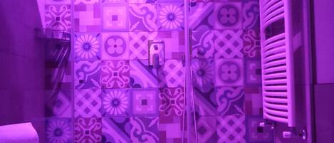 A bathroom with patterned tiles, a glass shower enclosure, a white sink, and a towel rack.