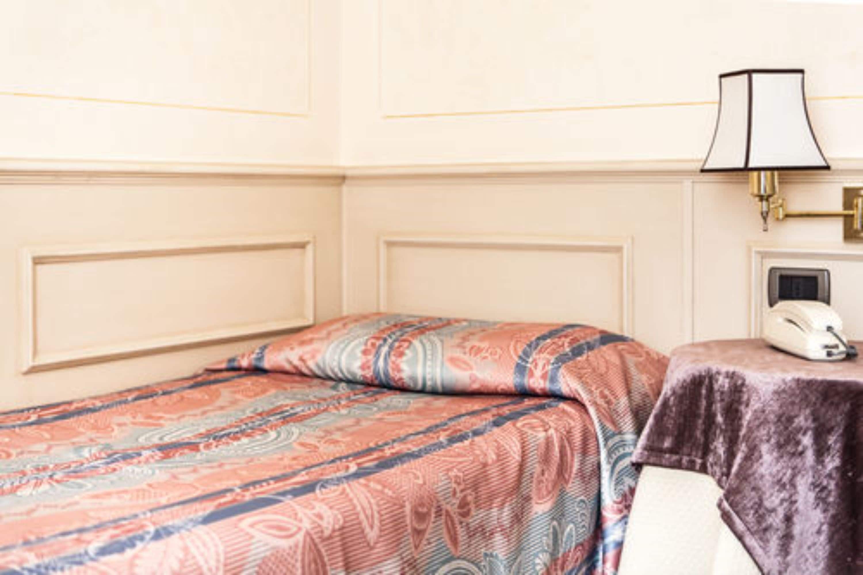 A hotel room with a bed, a bedside table with a lamp, and a telephone.