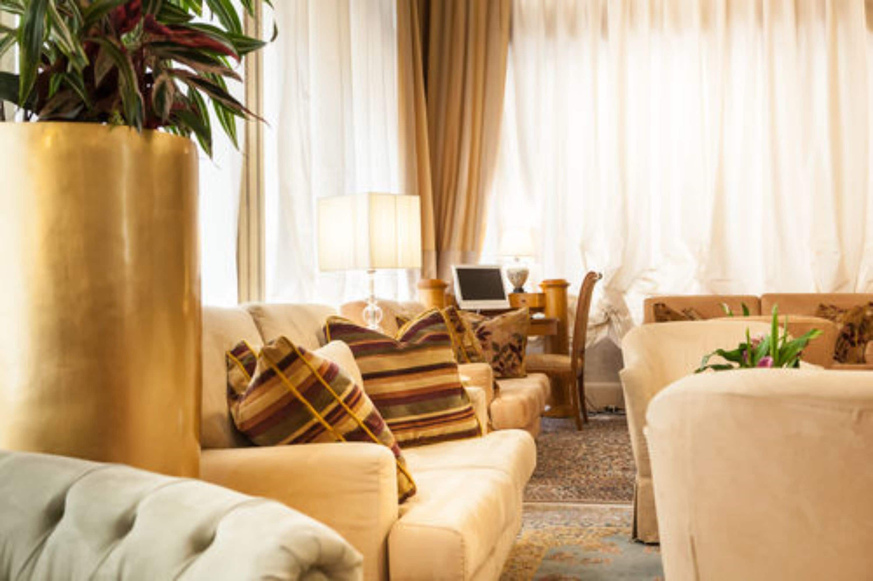 Una sala de estar acogedora con sofás color beige, un jarrón dorado grande y un ordenador portátil sobre una mesita auxiliar.