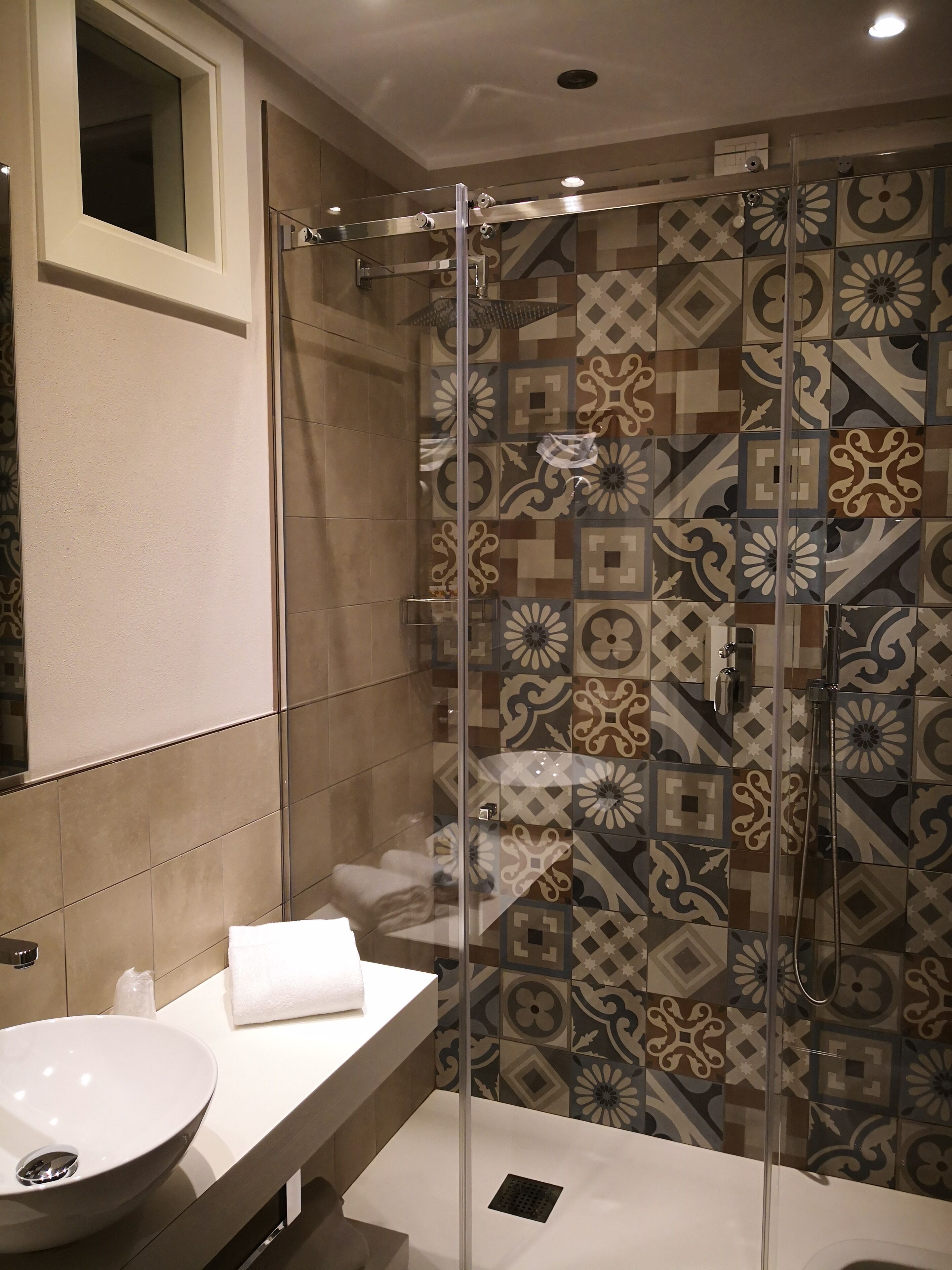 A modern bathroom with a glass-enclosed shower, a white sink, and patterned tiles.