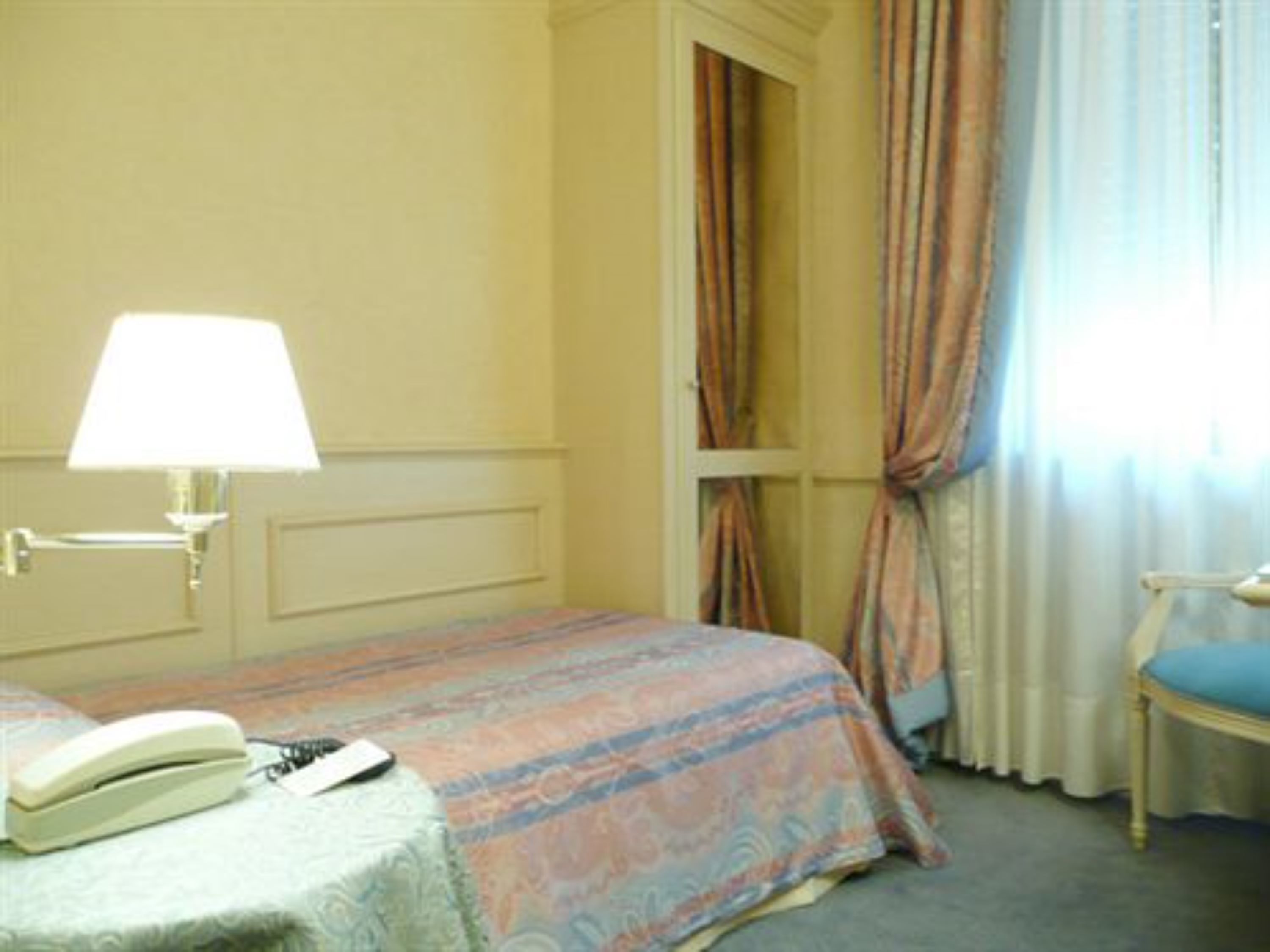 A hotel room with a bed, a bedside lamp, a chair, and a telephone on the bed.