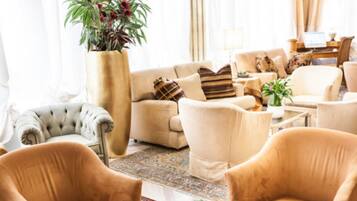 Ein Wohnzimmer mit einem beigen Sofa, Sesseln, einem Samtchesterfield-Sessel und einer großen Pflanze.