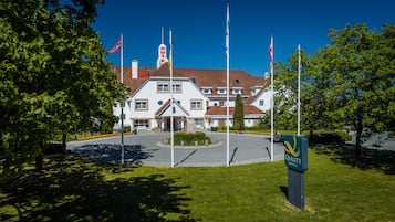 Stunning European-style hotel with a central entrance, surrounded by lush greenery and flags.