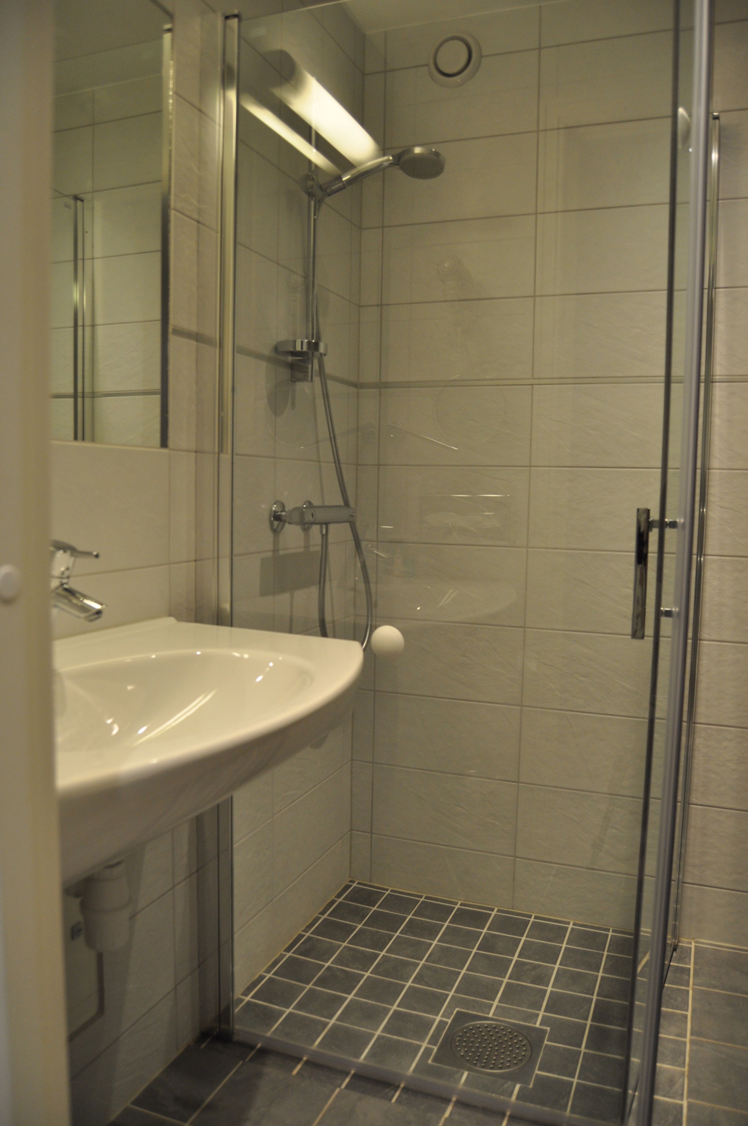 A modern bathroom with a glass-enclosed shower, a white sink, and tiled walls.