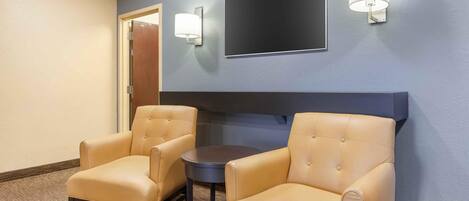 Una habitación con dos sillones de cuero, una mesita redonda pequeña, un televisor de pantalla plana montado en la pared y dos lámparas de pared.