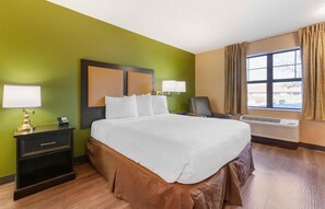 A hotel room with a large bed, bedside lamps, a chair, a desk with a phone, and a window with curtains.